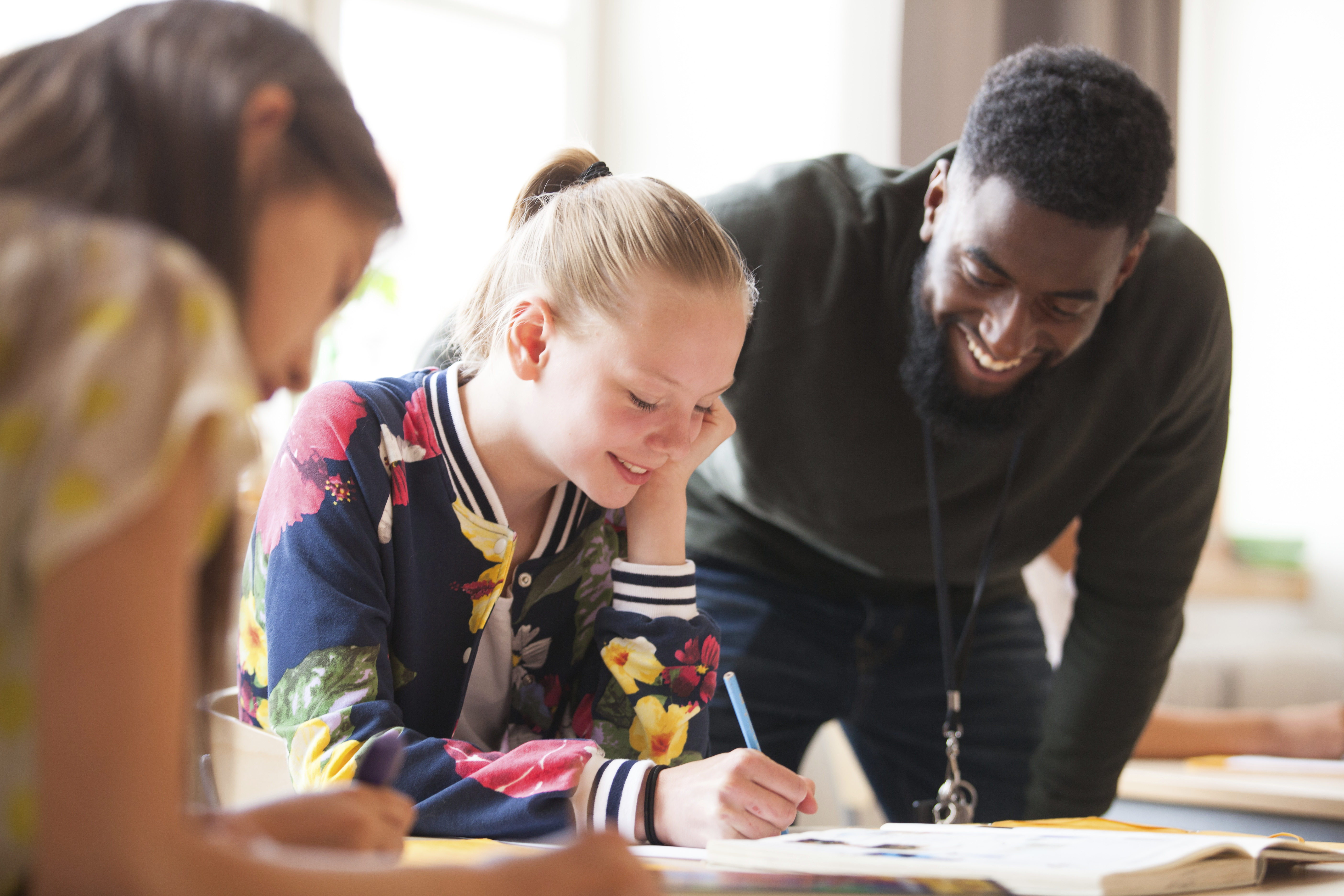 En lärare lutar sig ner för att hjälpa tre elever med sitt skolarbete